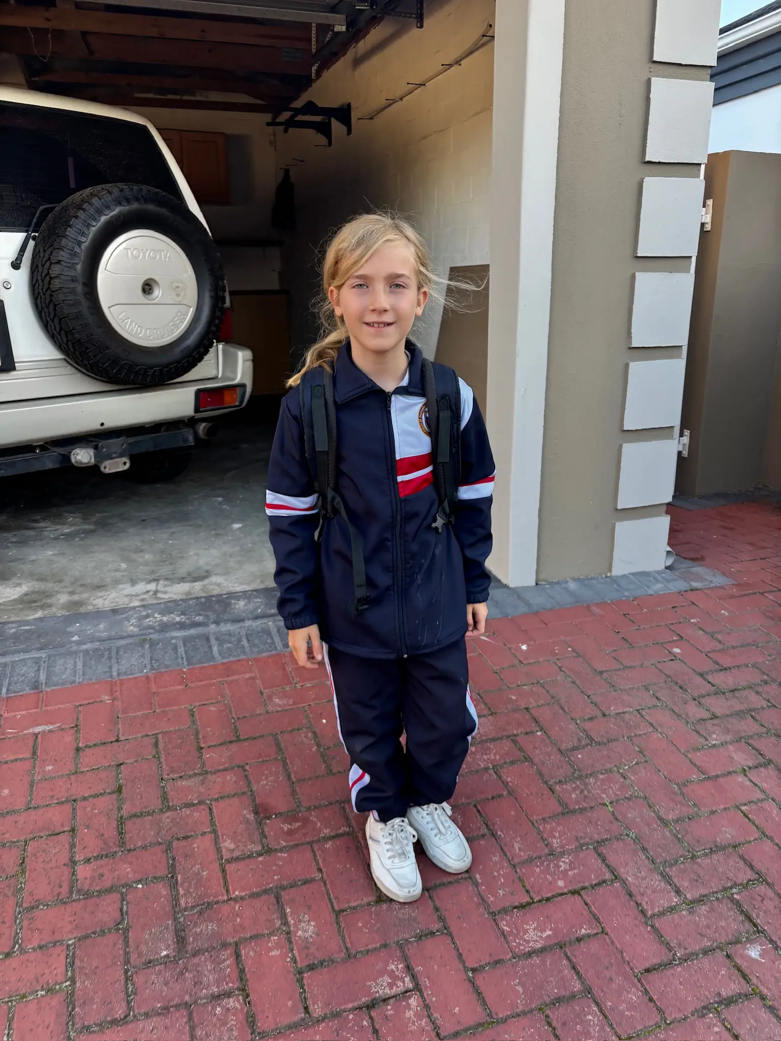 Merle mit Rucksack vor dem Haus, im Trainingsanzug